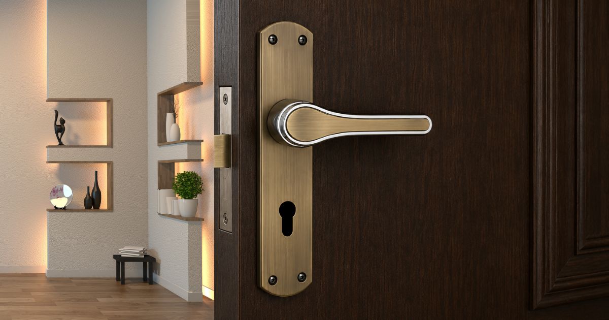Close-up of a brass lever door handle and keyhole on a dark wooden door, with a modern living room visible in the background.
