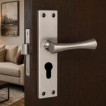 Close-up of a brushed metal door lever and keyhole plate on a dark wooden door, with a living room visible in the background.