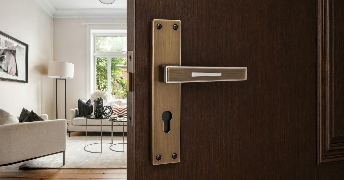 Door opens into a bright living room with beige sofa, black pillows, and a round glass coffee table by a window. The door features a brass lever handle.